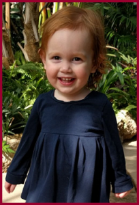 Une jeune fille aux cheveux roux souriant devant une plante. Elle s'appelle Alice.