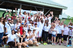 A group of Stroll participants pose for a photo in front of the Stroll for Liver banner, raising their hands in the air
