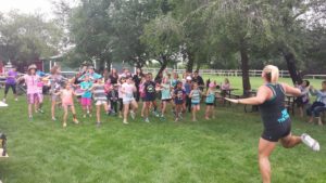 A group of children participating in the Stroll exercise with an instructor on a field of grass