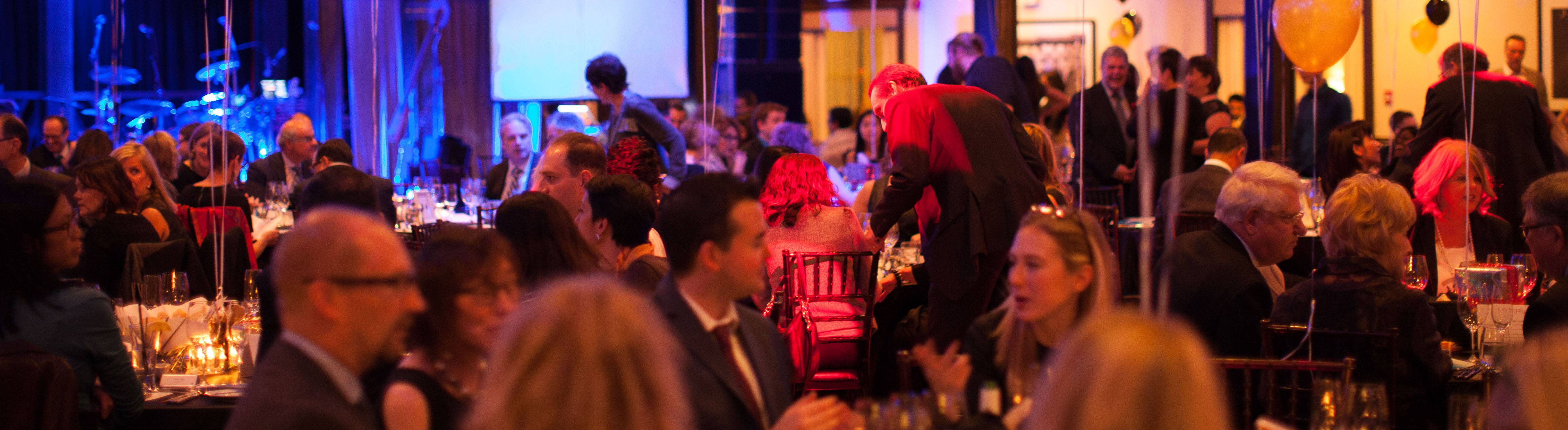 A view of the Gala room, with people sitting around tables and black and gold balloons in the air