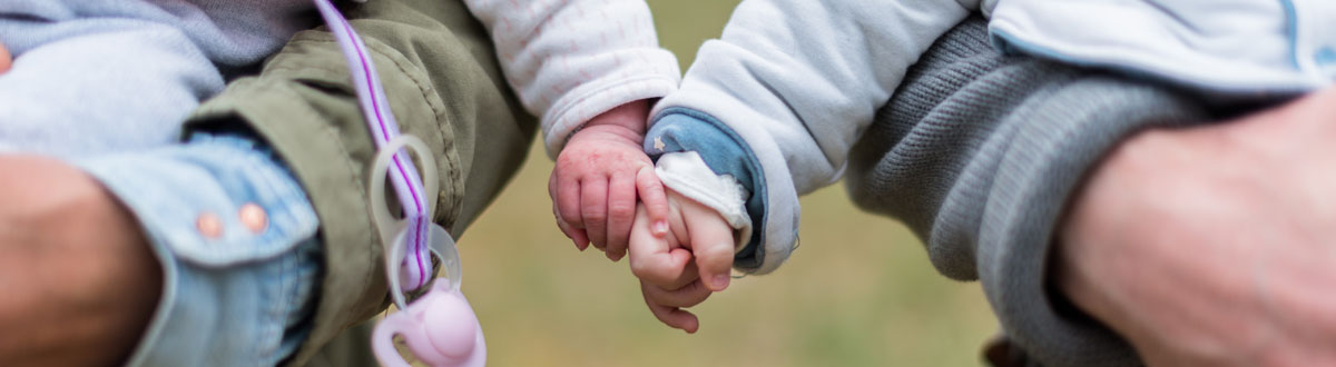 Two young children, being held by their parents, hold hands with each other