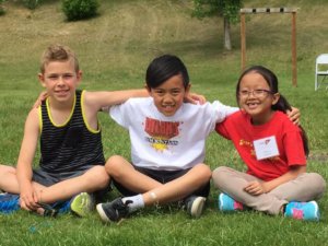 Trois enfants sont assis les jambes croisées sur un champ d'herbe, les bras l'un autour de l'autre