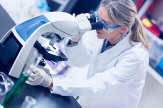 Female Researcher looking through microscope in lab coat
