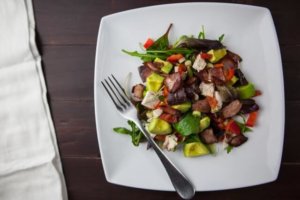A balanced diet of fruit, vegetables, meat and dairy work wonders on your liver health. This is a plate of a mixed salad with avocado, tomato, chicken and a soft cheese.