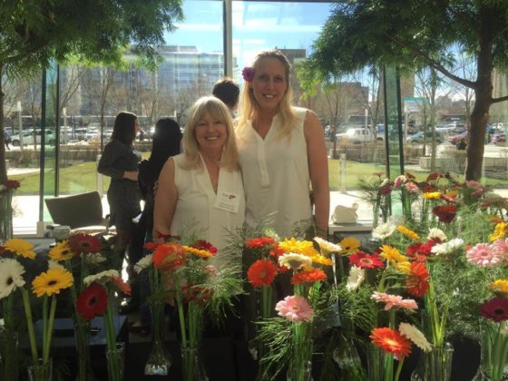 Marla and Debralee pose in front of flowers for sale. 