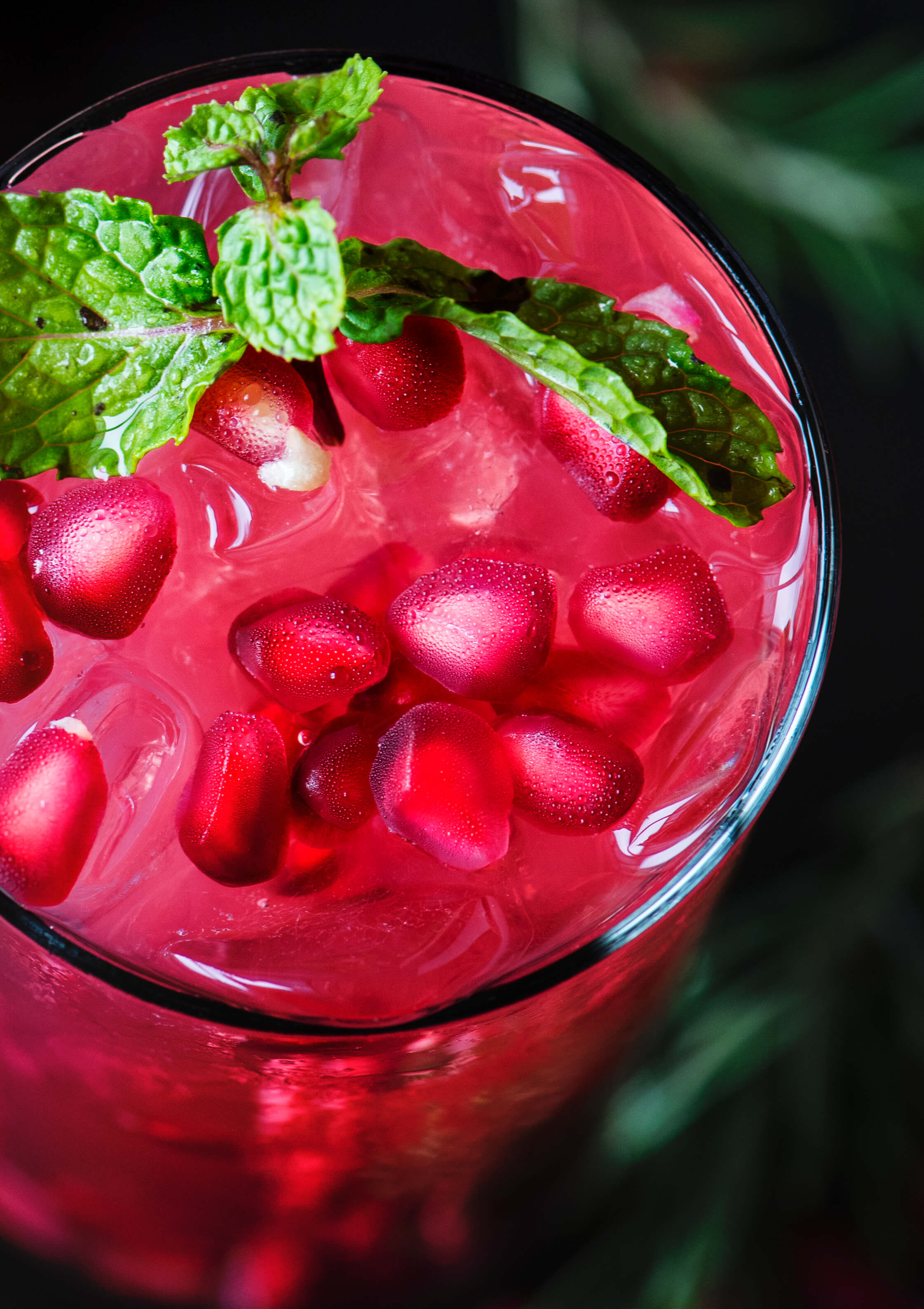 Pomegranate grape punch served cold, garnished with a mint sprig and pomegranate seeds.