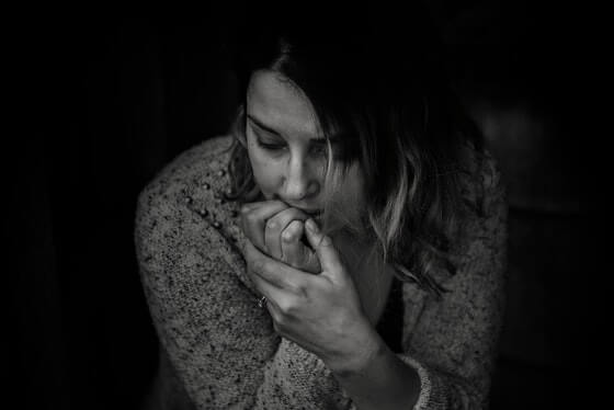 A black and white image of a woman looking worried, biting her nails and looking off into the distance.
