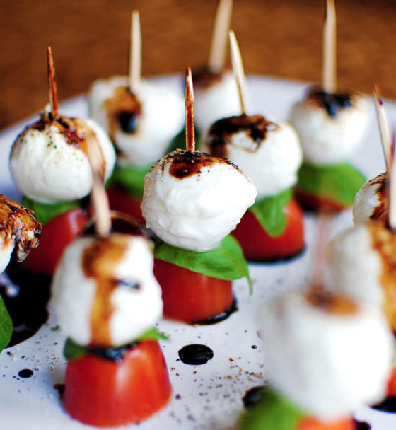 A dish is shown with rows of tomatoes, basil leaves, mozzarella balls on toothpicks