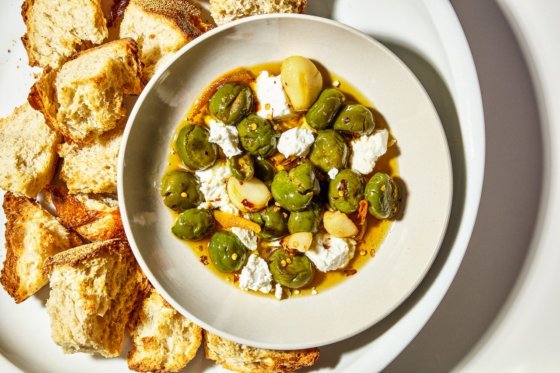A plate with crusted bagitini bread is arranged around a bowl of olives, feta, olive oil and garlic to be dipped in.