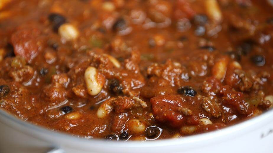 A close up of a pot of chili cooking in a slow cooker. The stew is a deep red or brown colour, and you can see ground turkey, black beans, kidney beans and corn. 