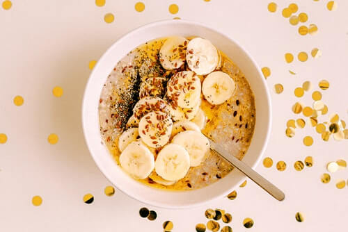 A bowel of oatmeal topped with slices of banas, seeds and cinnamon. Around the bowl are small circles of sparkly sequences for decoration. 
