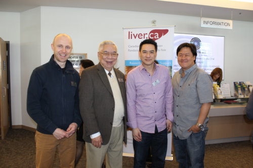 Four men pose together smiling outside of the information desk at one of the LIVERight Health Forums. Behind them, a Canadian Liver Foundation banner can be partially seen with the logo exposed. 